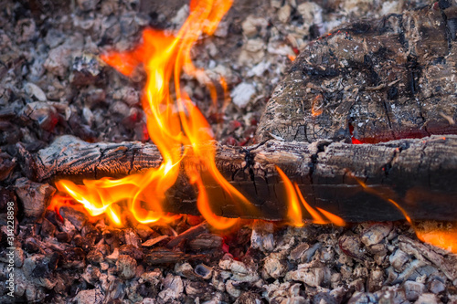 Tongues of flame on a background of dark gray coals. Firewood burning in a brazier on a bright yellow flame. Closeup. Copy space.