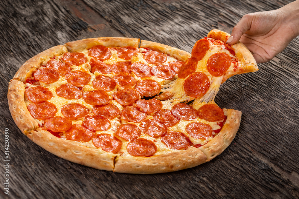 Hot pepperoni pizza ready to eat. Very cheesy pizza slice in hand on old wooden table