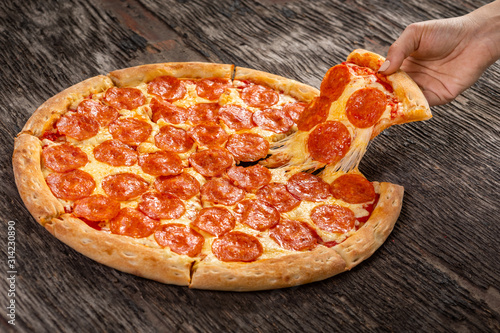 Obraz na płótnie Hot pepperoni pizza ready to eat. Very cheesy pizza slice in hand on old wooden table w salonie