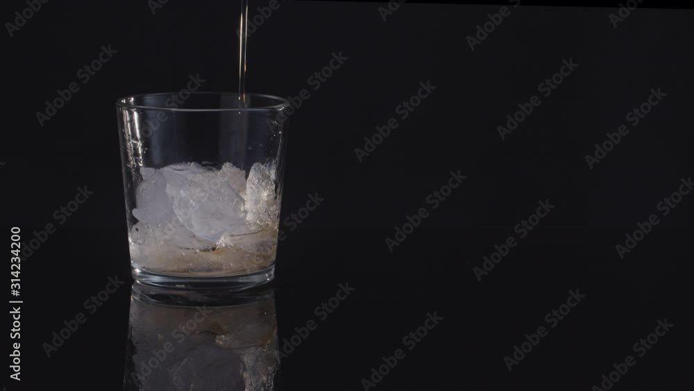 close-up in a glass with ice pour whiskey on a black background close-up in a glass with ice pour whiskey on a black background