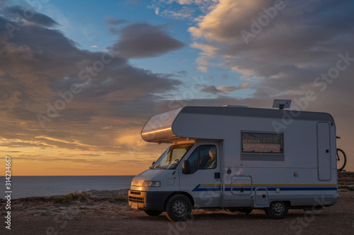 sunset / sunrise at rocky seaside with travel trailer with bike. Dramatic and calm cloudy sky with sun beams