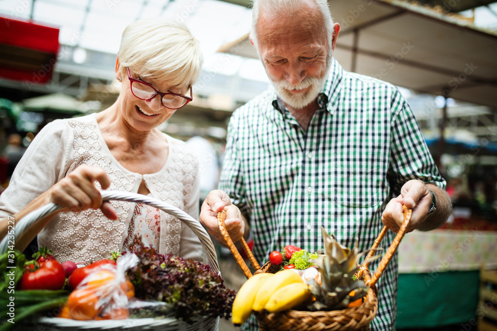 Smiling senior couple holding basket with vegetables at the market Smiling senior couple holding basket with vegetables at the market