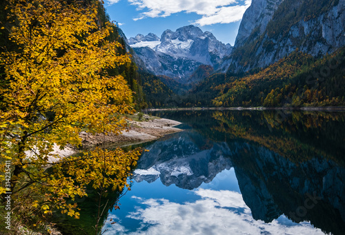 Peaceful autumn Alps mountain lake with clear transparent water and reflections. Gosauseen or Vorderer Gosausee lake, Upper Austria. Dachstein summit and glacier in far.