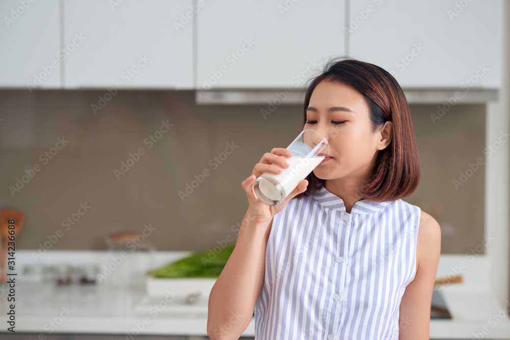 Portrait of young Asian woman drinking milk while standing in the kitchen. Portrait of young Asian woman drinking milk while standing in the kitchen.