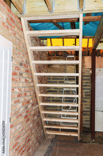 Indoor renovation project. Temporaty wooden staircase, brick wall, unfinished roof, selective focus