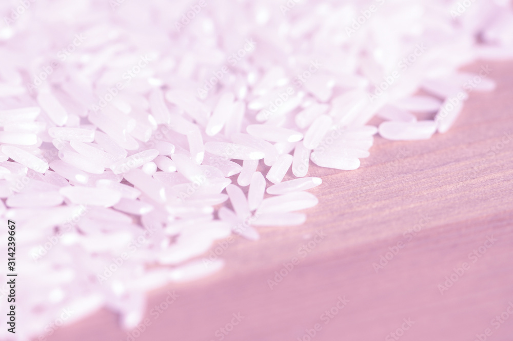 Obraz premium White rice grains scattered on a wooden surface close up. Food background pink color toned