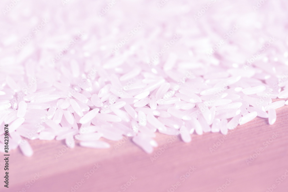 Obraz premium White rice grains scattered on a wooden surface close up. Food background pink color toned