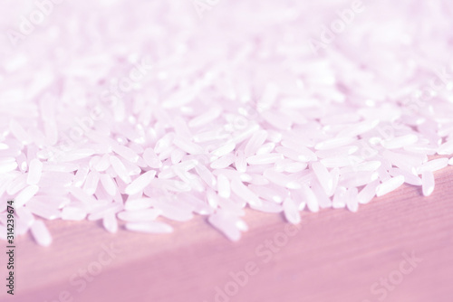 White rice grains scattered on a wooden surface close up. Food background pink color toned