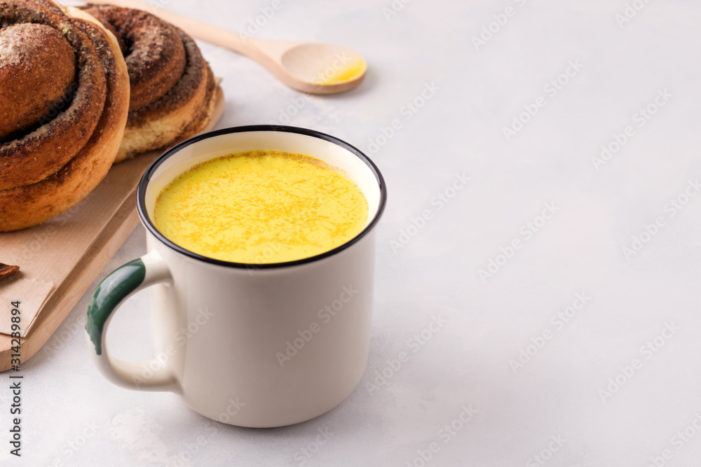 Indian turmeric drink with golden milk on a white plate next to buns with koice. Have copy space Indian turmeric drink with golden milk on a white plate next to buns with koice. Have copy space