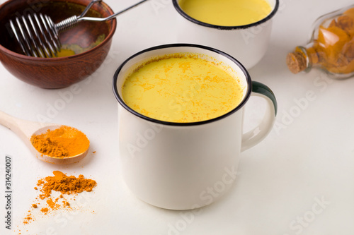 two mugs of golden milk next to turmeric on a white table