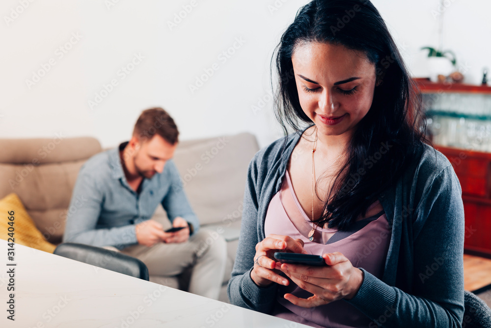 close up photo of a beautiful woman using a mobile phone at home - friend or boyfriend out of focus in background texting with a smartphone - millennials lifestyle close up photo of a beautiful woman using a mobile phone at home - friend or boyfriend out of focus in background texting with a smartphone - millennials lifestyle
