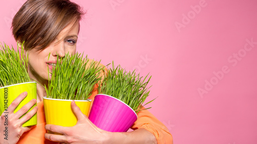 Photos Young beautiful woman with wheatgrass in flower pots over brigh pink background