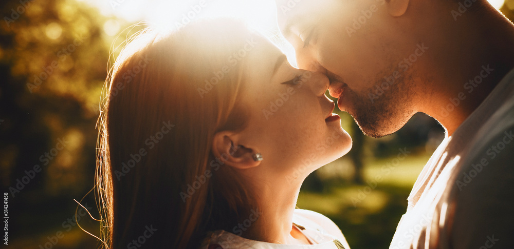 Close up portrait of a lovely young couple smiling before kissing against sunset with closed eyes outdoor in the park while dating.