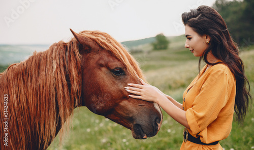 Obraz na plátně Side view portrait of a lovely young female touching a horse in the mountains while traveling