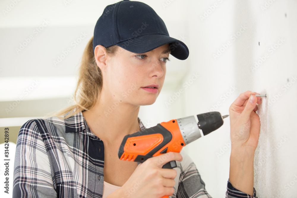 woman builder drilling on the wall