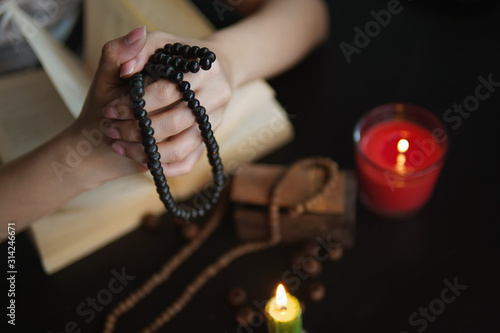 Bild auf Leinwand Young Woman Pray Carrying a rosary necklace on hand near black wooden table with open Bible, she sitting next to a burning candle in room