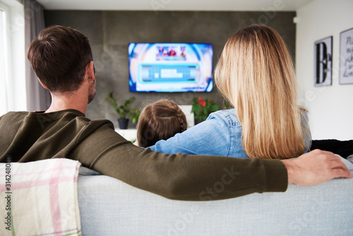 Rear view of family watching tv in living room