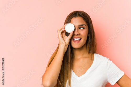 Young caucasian woman holding a mousturizer isolated on a pink background