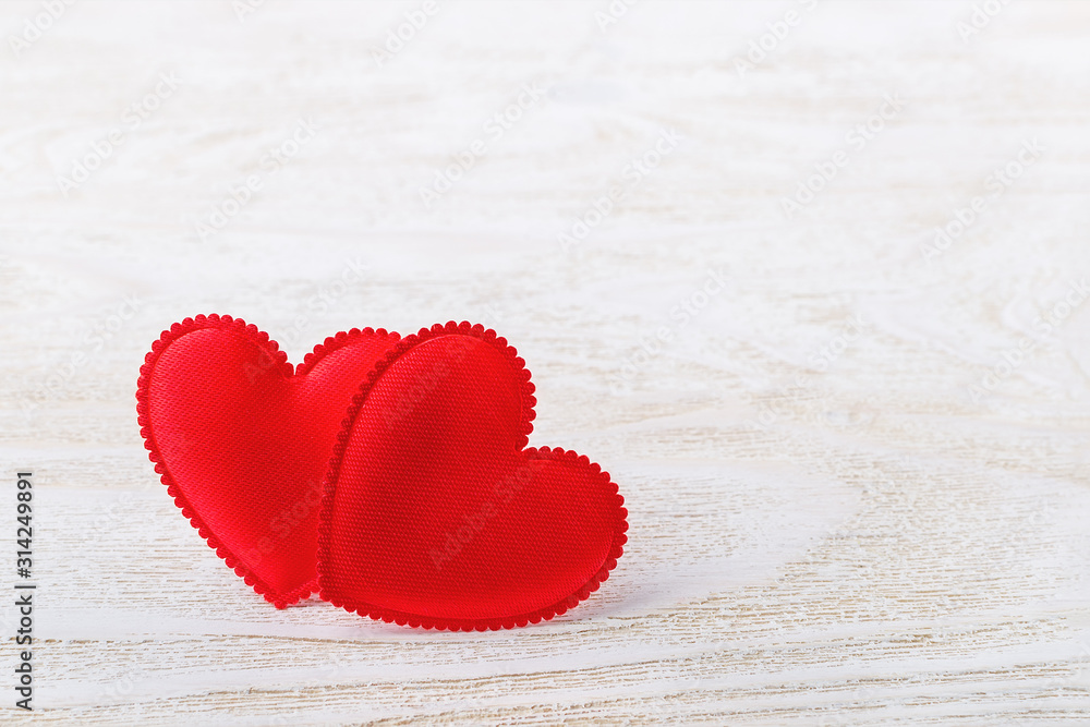 Fototapeta premium Two red silk valentine hearts on a white wooden textured background. Concept love, Valentine's day. Greeting card with copy space.