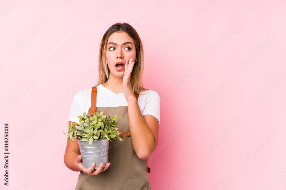 Young caucasian gardener woman in a pink background is saying a secret hot braking news and looking aside Young caucasian gardener woman in a pink background is saying a secret hot braking news and looking aside