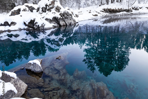 Landmark in the mountains of Altai, blue lakes non-freezing in winter around stones with green silt covered with snow in which trees and sky are reflected.
