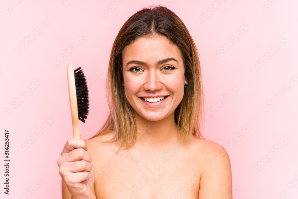 Young caucasian woman holding a hairbrush isolated happy, smiling and cheerful. Young caucasian woman holding a hairbrush isolated happy, smiling and cheerful.