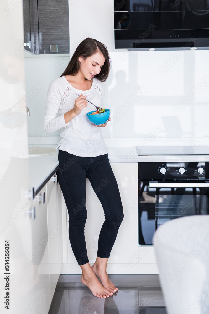 Charming young woman eating salad in the kitchen Charming young woman eating salad in the kitchen