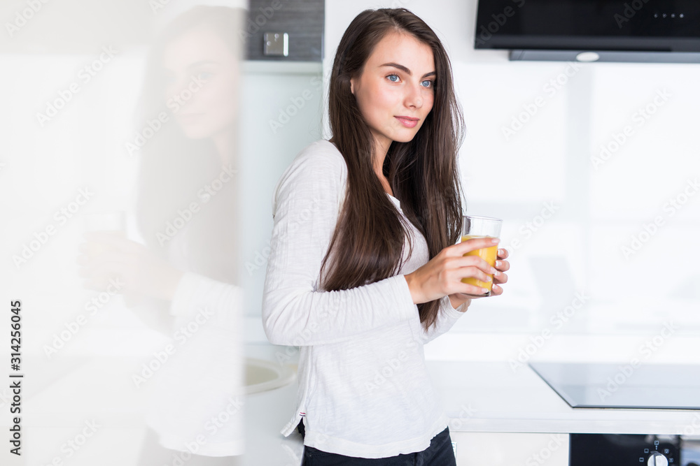 Attractive woman holding a glass of orange juice while standing in the kitchen Attractive woman holding a glass of orange juice while standing in the kitchen