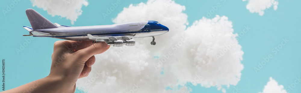 cropped view of woman playing with toy plane among white fluffy clouds made of cotton wool isolated on blue, panoramic shot - obrazy, fototapety, plakaty 