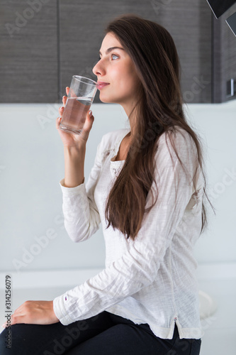 Beautiful young woman drink and holds a glass with water on kitchen