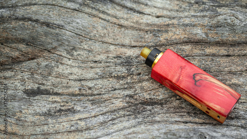 high end red natural stabilized wood regulated box mods with rebuildable dripping atomizer on natural timber wood texture background, vaporizer equipment, selective focus