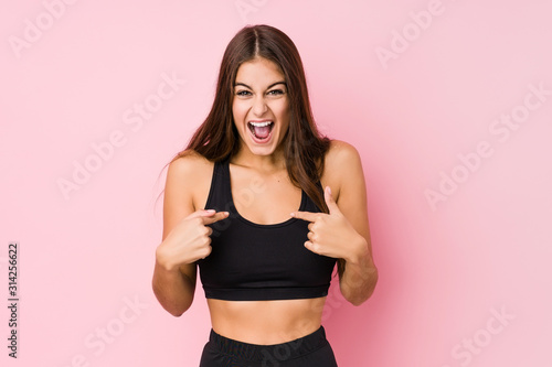 Young caucasian fitness woman doing sport isolated surprised pointing with finger, smiling broadly. © Asier