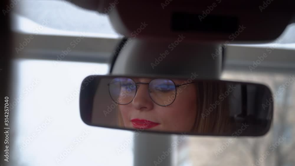 Beautiful woman with glasses looks in the rearview mirror in the car Beautiful woman with glasses looks in the rearview mirror in the car