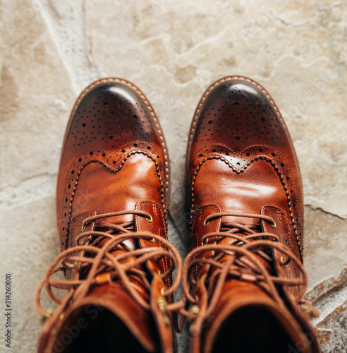 A pair of Brown natural leather medium boots with unlaced shoelaces standing on natural stone floor top view. photo