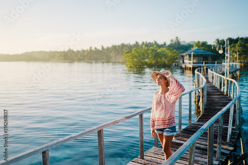 Vacation on tropical island. Young woman in hat enjoying sunset sea view from wooden bridge terrace, Siargao Philippines.