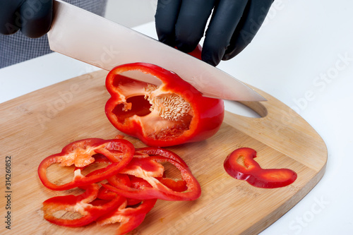 chef's hands cut fresh slices of red pepper on a bamboo board.