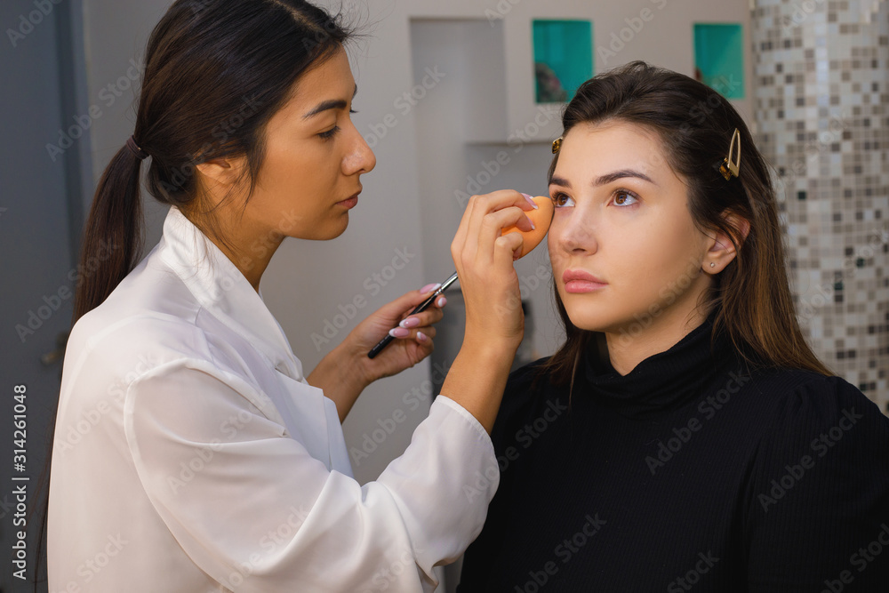 Make-up artist in the process of creating trendy nude makeup. Girls of Caucasian appearance with long hair and well-groomed looks Make-up artist in the process of creating trendy nude makeup. Girls of Caucasian appearance with long hair and well-groomed looks