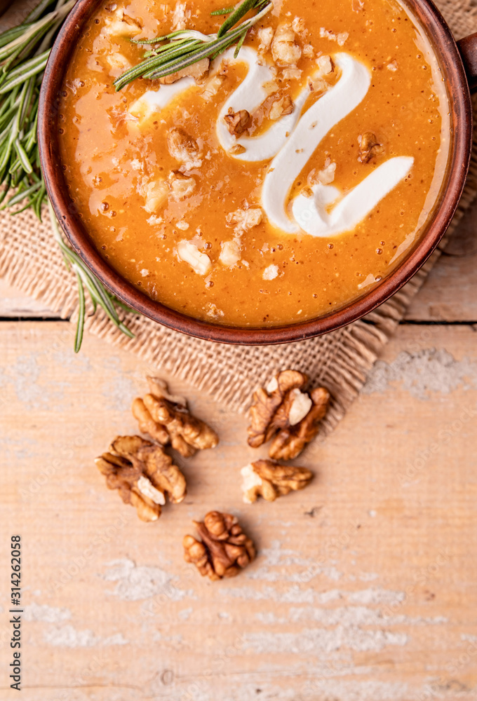 Fototapeta premium Pumpkin soup with creme in brown bowl decorated with walnuts top view with copy space on wooden background