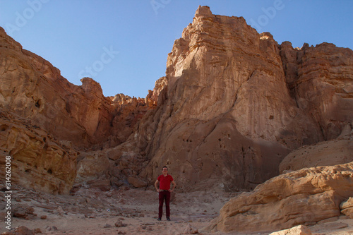 Caucasian male traveler in a red T-shirt posing against the backdrop of a sandy rock in the Timna National Park, Israel