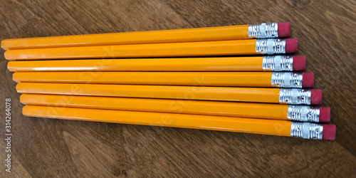Group of yellow penciles lined up on a wood desk.