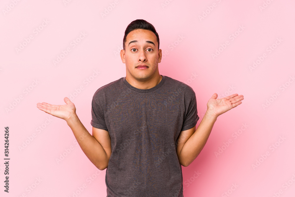 Yooung latin man posing in a pink backgroundconfused and doubtful shrugging shoulders to hold a copy space. Yooung latin man posing in a pink backgroundconfused and doubtful shrugging shoulders to hold a copy space.
