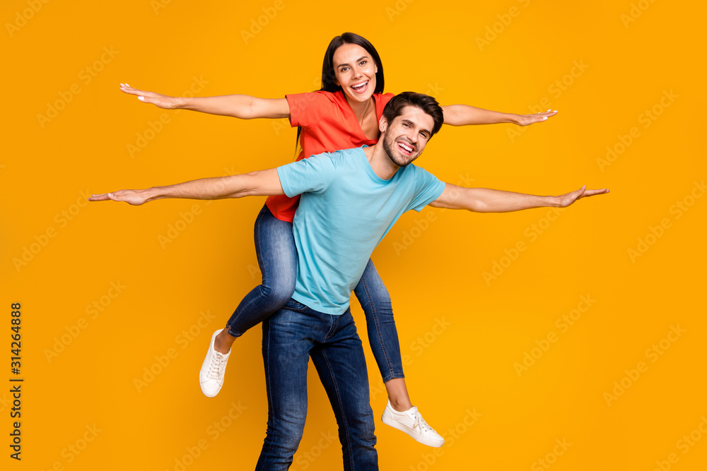 Photo of two funny people guy carry lady piggyback meet summer time together spread hands like wings wear casual stylish blue orange t-shirts jeans isolated yellow color background Photo of two funny people guy carry lady piggyback meet summer time together spread hands like wings wear casual stylish blue orange t-shirts jeans isolated yellow color background