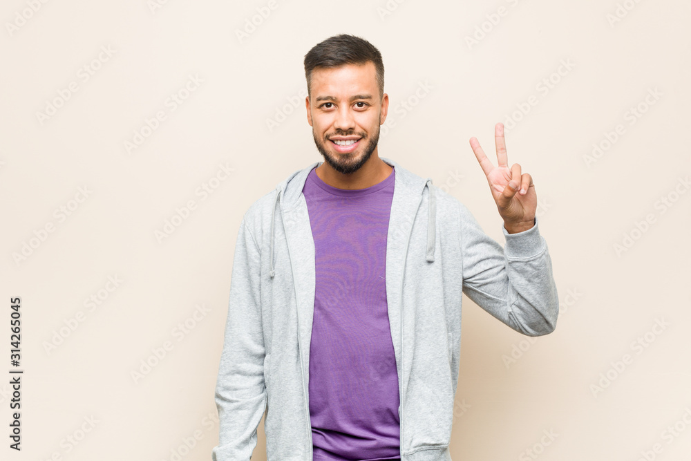 Young south-asian man joyful and carefree showing a peace symbol with fingers. Young south-asian man joyful and carefree showing a peace symbol with fingers.