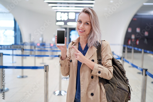 Travel and technology. Online check-in. Female traveler showing smartphone waiting for boarding near registration desk line.