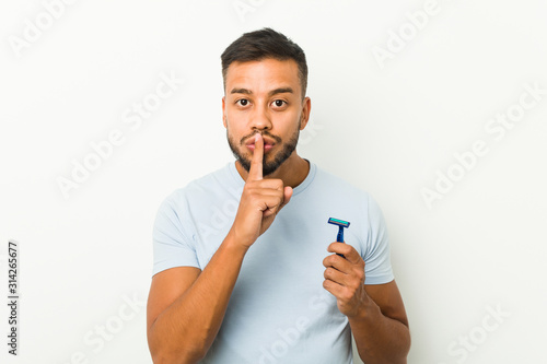 Young south-asian man holding a razor blade keeping a secret or asking for silence.