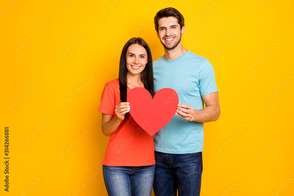 Photo of amazing two people guy lady celebrating valentine day holding red paper heart figure shape wear casual blue orange t-shirts isolated yellow color background