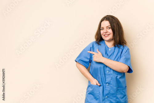 Young curvy nurse woman smiling and pointing aside, showing something at blank space.