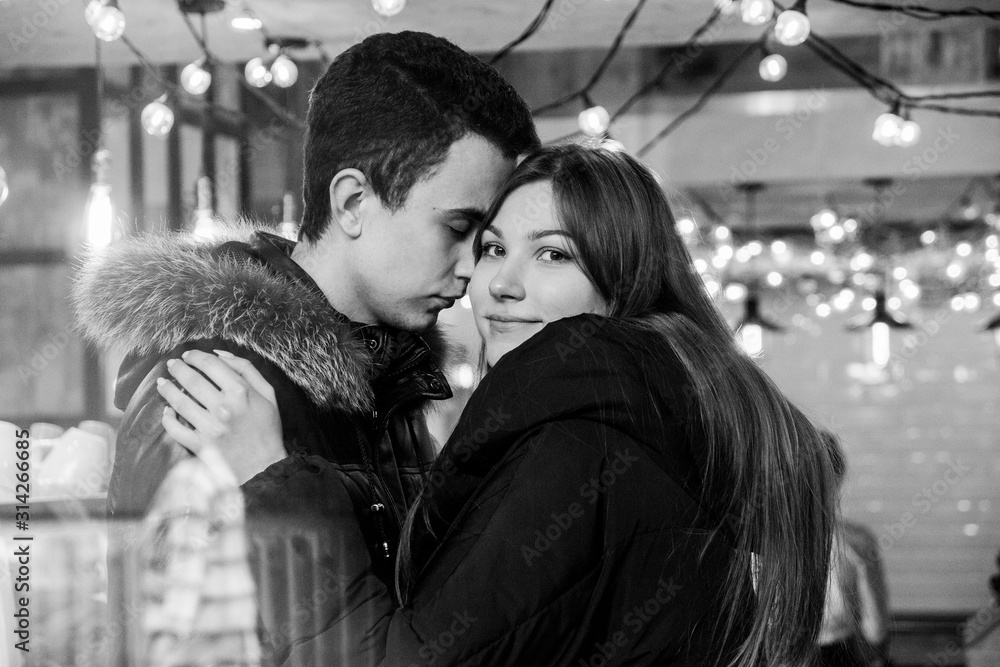 Cute smiling couple in love standing in a cafe hugging each other, image through the glass Cute smiling couple in love standing in a cafe hugging each other, image through the glass