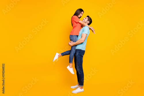 Full body photo of two cute people couple guy holding carrying lady look eyes lovely weekend romance moment wear casual blue orange t-shirts jeans isolated yellow color background