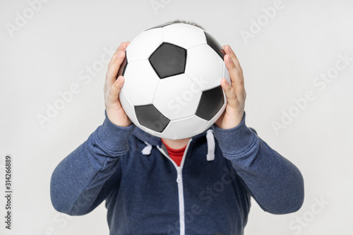 Man holding soccer ball on the face place. Casual wear, studio, isolated on light background, concept. trend subject covers a person face.